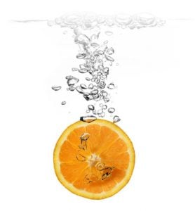 An orange slice being dropped in water to clean it.
